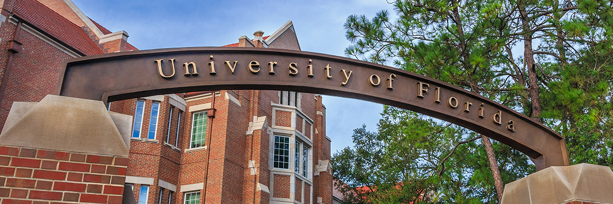 University of Florida sign over a gate with a brick building in the background